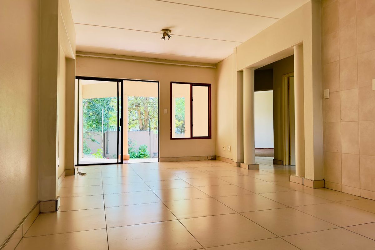 An empty, open-plan living area featuring tiled flooring, structural columns, and a sliding glass door providing access to the outdoor space.