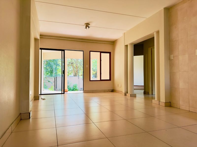 An empty, open-plan living area featuring tiled flooring, structural columns, and a sliding glass door providing access to the outdoor space.