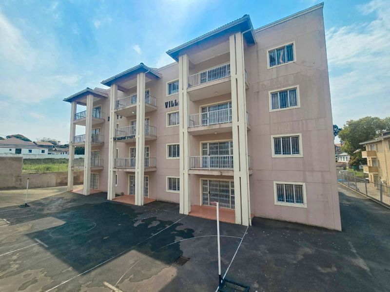 Exterior view of a multi-story apartment building featuring private balconies, security gates, and a paved courtyard area.