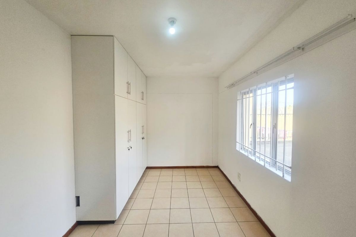 An empty bedroom featuring tiled flooring, built-in cupboards, and a window fitted with security bars.