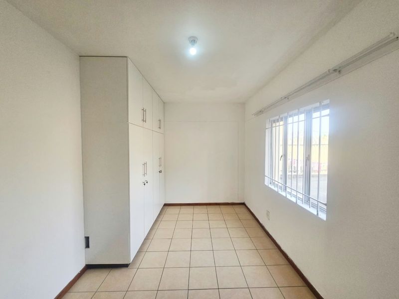 An empty bedroom featuring tiled flooring, built-in cupboards, and a window fitted with security bars.