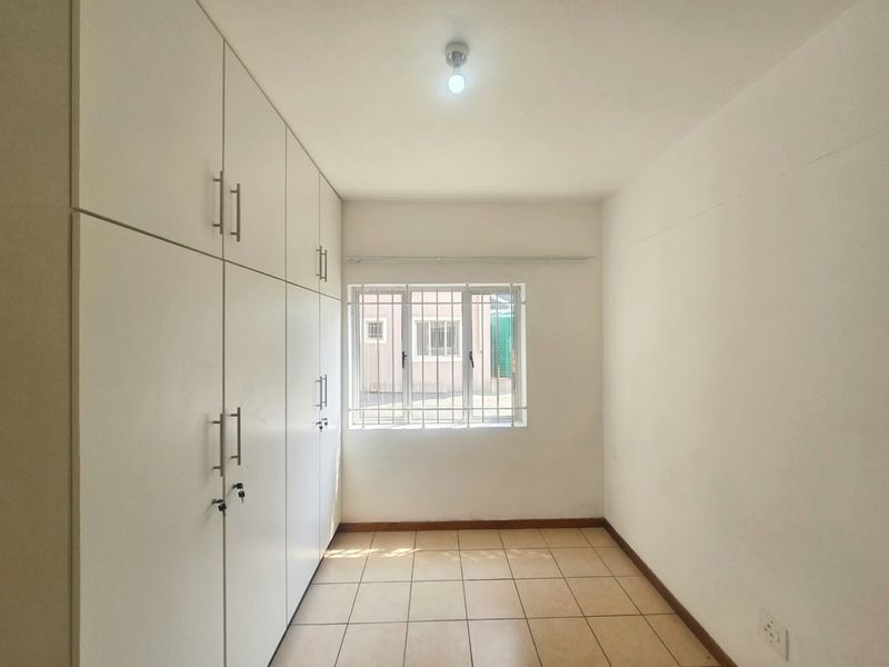 A clean, empty bedroom featuring neutral tiled flooring and extensive built-in cupboard storage with a window fitted with security bars.