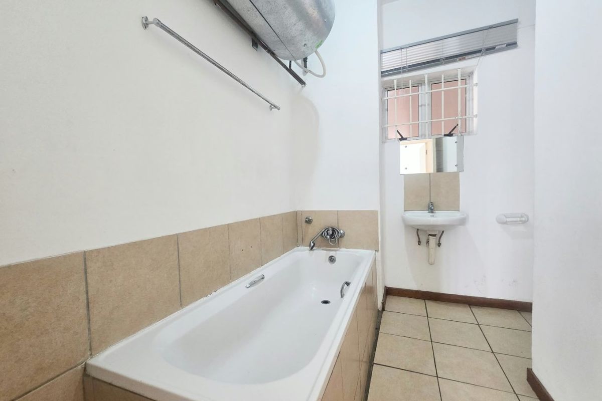 A functional bathroom featuring a bathtub, wall-mounted basin, and tiled finishes, currently awaiting modernization to improve its aesthetic appeal.