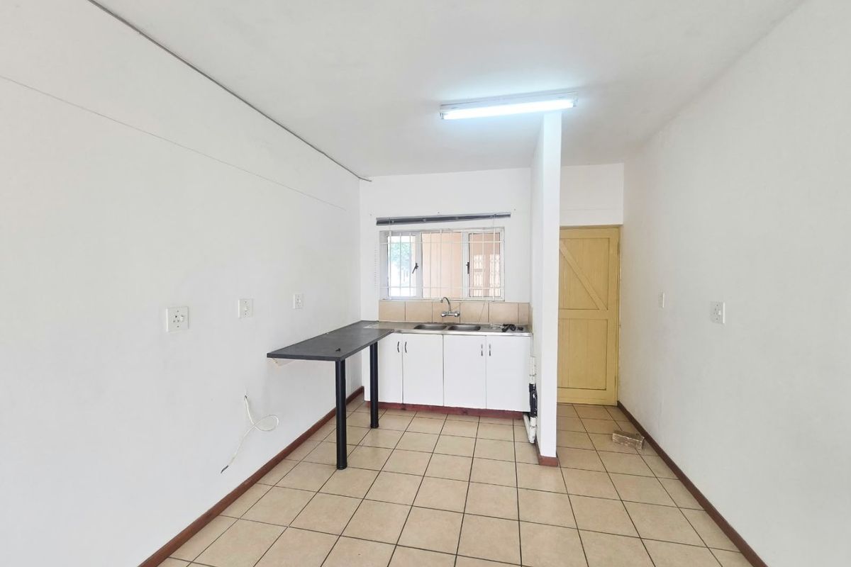 A compact, empty kitchen area featuring basic cabinetry, a double sink, tiled flooring, and security bars on the window.