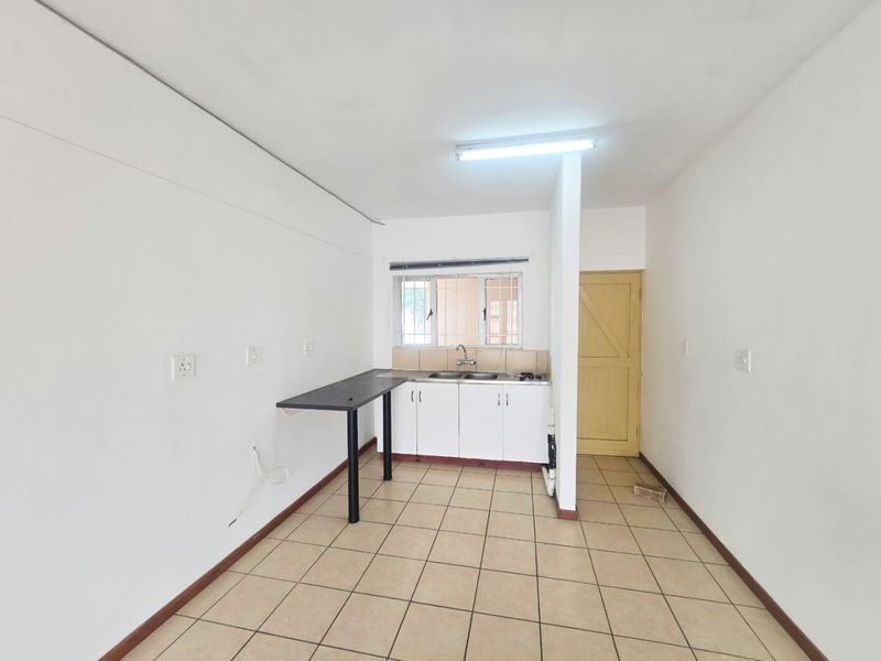A compact, empty kitchen area featuring basic cabinetry, a double sink, tiled flooring, and security bars on the window.