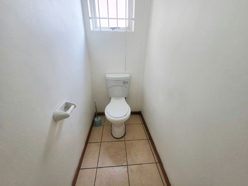 A compact, functional guest toilet featuring tiled flooring and a small window with security bars.