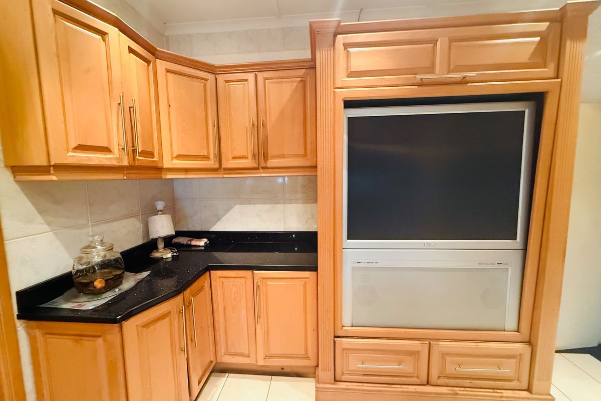 A kitchen area featuring wooden cabinetry, granite countertops, and a built-in entertainment unit, offering a functional layout with tiled finishes.