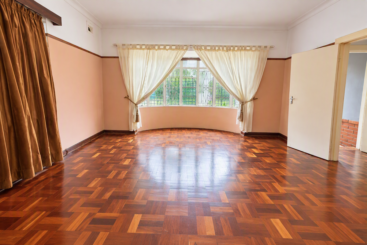A spacious, empty living room featuring polished parquet flooring, a large bay window with security bars, and classic picture rail detailing.