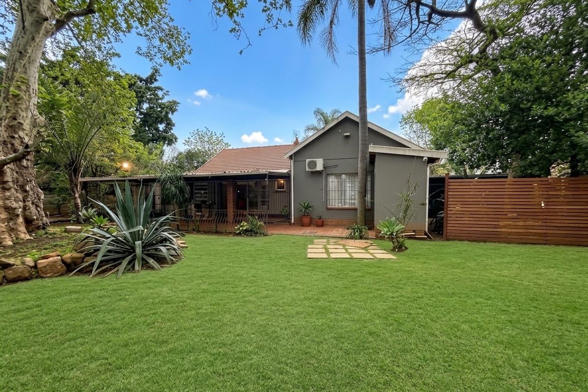 A well-maintained rear exterior view of the townhouse featuring a spacious lawn, a covered patio area, and established garden landscaping.