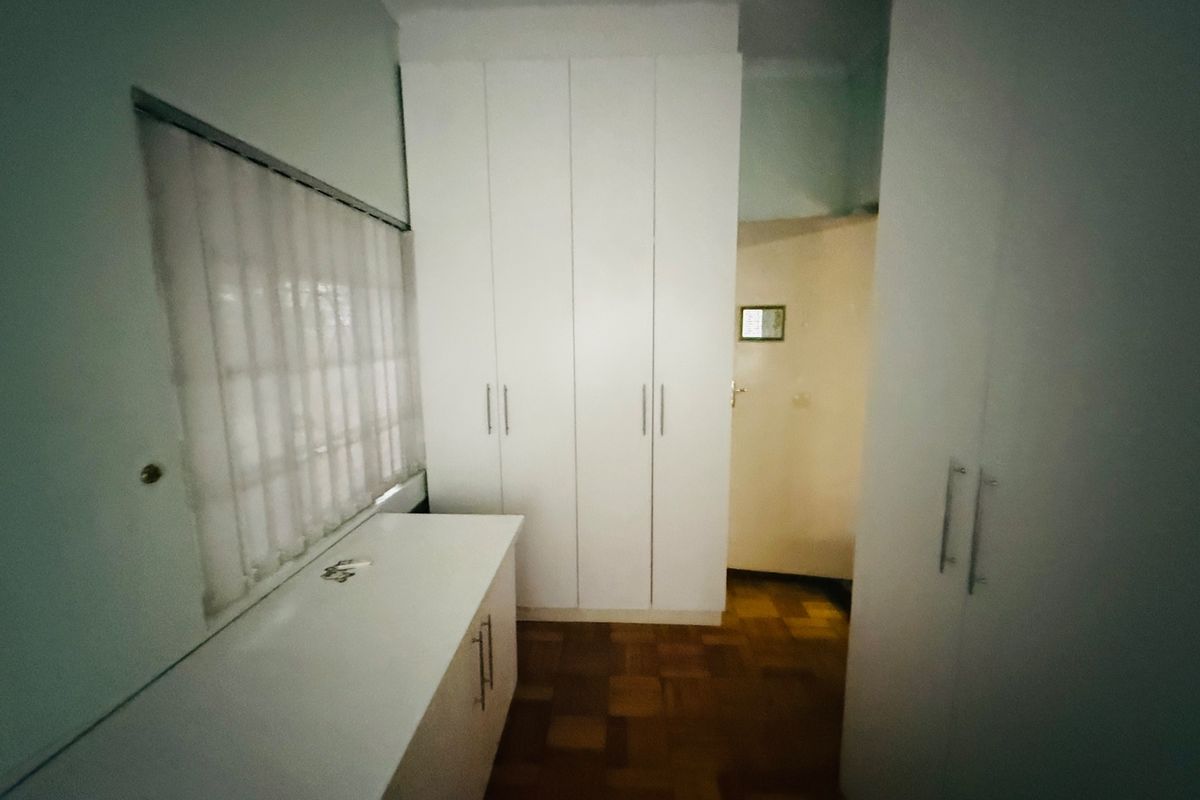 A bedroom featuring parquet flooring, extensive built-in white cupboards, and a built-in vanity unit with a window.