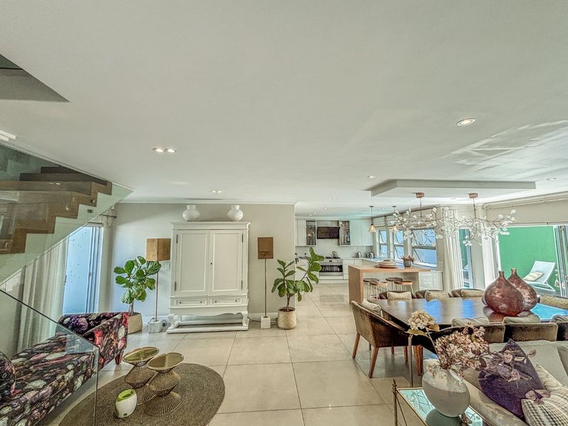 Spacious open-plan living and dining area featuring tiled floors, a modern kitchen with an island, and a contemporary glass-railed staircase.