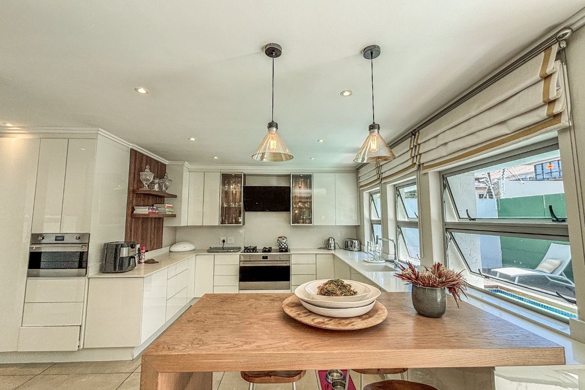 Modern kitchen featuring high-gloss cabinetry, stone countertops, built-in oven, gas hob, and stylish pendant lighting, offering a clean and functional culinary space.