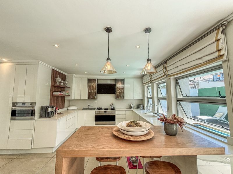 Modern kitchen featuring high-gloss cabinetry, stone countertops, built-in oven, gas hob, and stylish pendant lighting, offering a clean and functional culinary space.