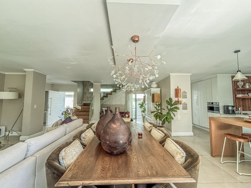 Spacious open-plan living and dining area featuring modern cabinetry, a built-in oven, and a striking staircase with a glass balustrade.