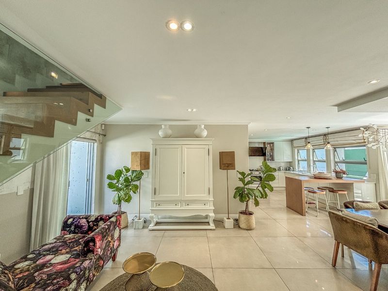 Spacious open-plan living area featuring a modern glass staircase, polished floor tiles, and a contemporary kitchen with a central island.