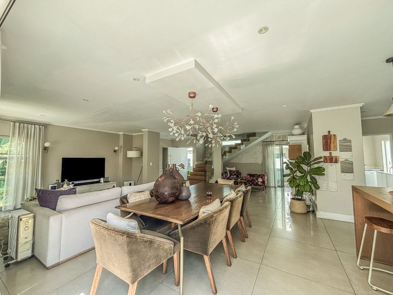 Spacious open-plan living and dining area featuring tiled floors, a modern feature ceiling bulkhead, and a staircase with a glass balustrade.