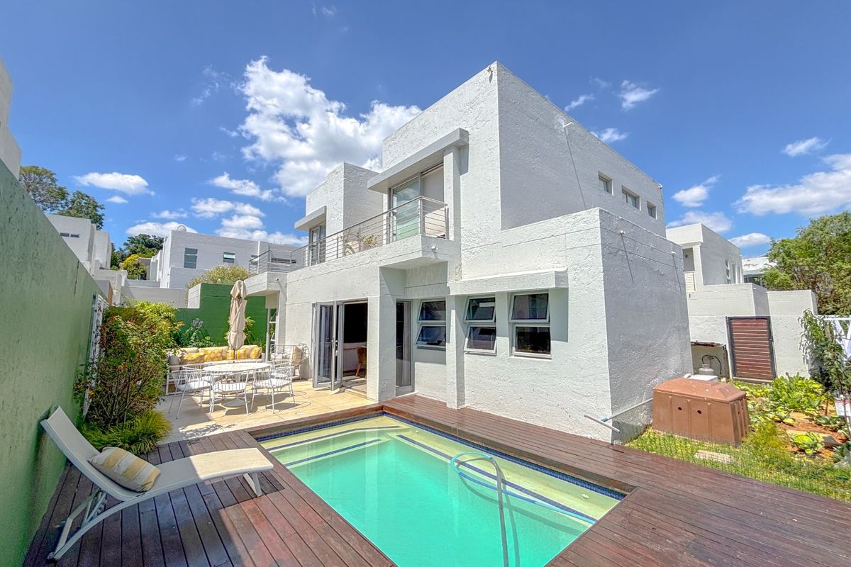 Rear exterior view of a modern multi-level home featuring a swimming pool, timber decking, and a private balcony.