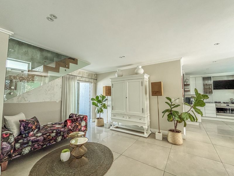 Spacious open-plan living area featuring large format floor tiles, a modern glass staircase balustrade, and a seamless transition to a contemporary kitchen.