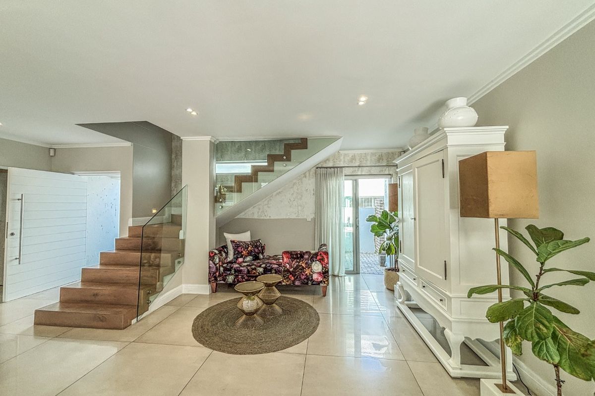 Spacious living area featuring a modern timber staircase with glass balustrade, polished porcelain floor tiles, and direct access to the rear patio.