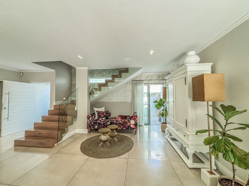 Spacious living area featuring a modern timber staircase with glass balustrade, polished porcelain floor tiles, and direct access to the rear patio.