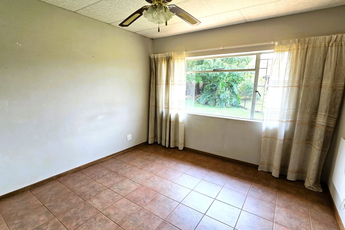 An empty bedroom featuring tiled flooring, a ceiling fan, and a large window overlooking the garden.
