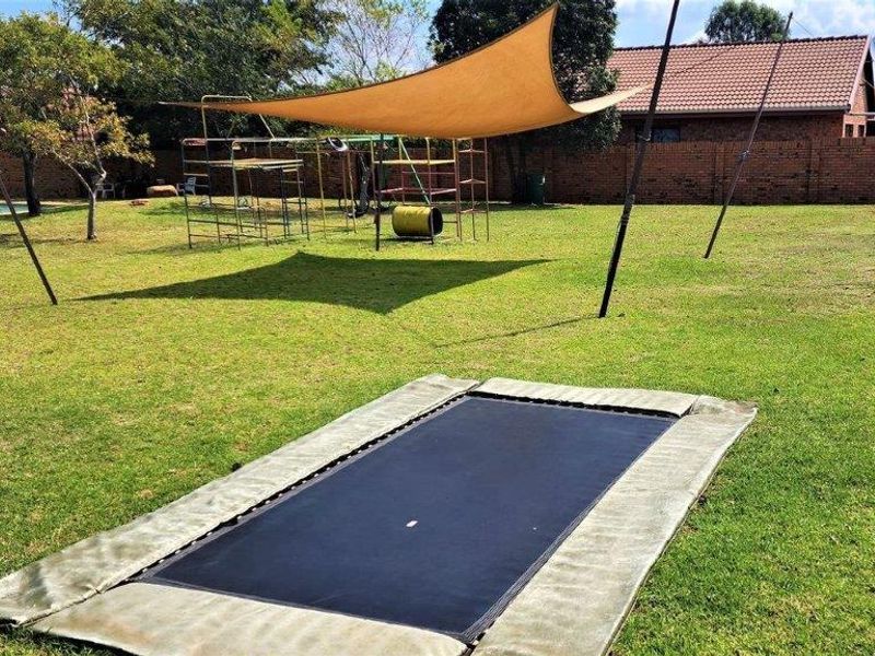 Spacious backyard featuring a large lawn, in-ground trampoline, shade sail structure, and a swimming pool, enclosed by a brick boundary wall.