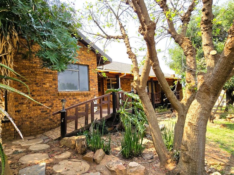 A rear view of the house featuring a face brick facade, a raised timber deck with a handrail, and a mature landscaped garden.