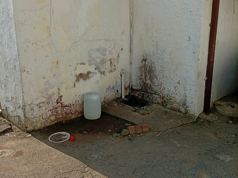 An exterior rear area showing significant wear to the wall plaster and paint, featuring an external water tap and drainage point.
