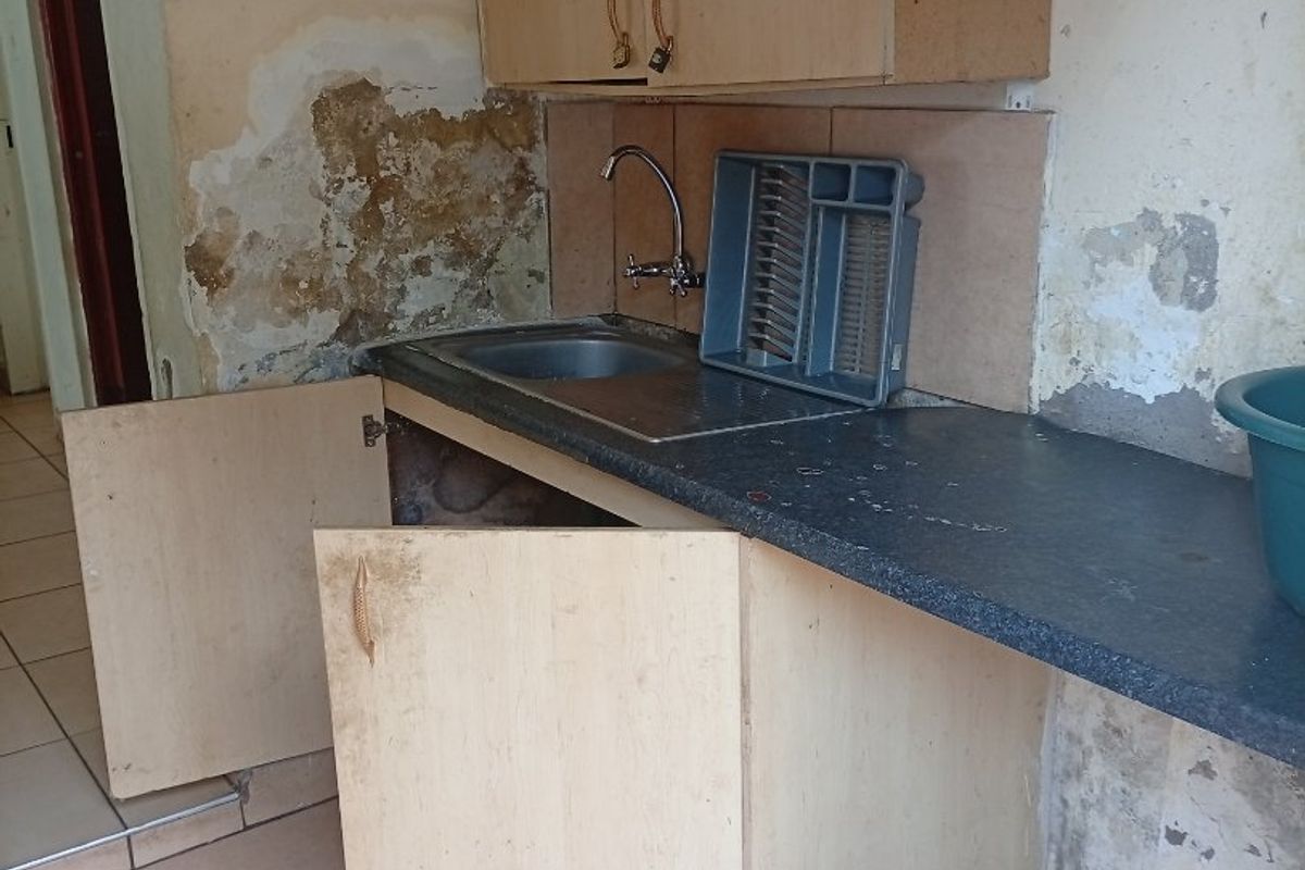 A small kitchen area featuring basic cabinetry and a sink, currently showing significant wall damage and requiring extensive renovation and repair.