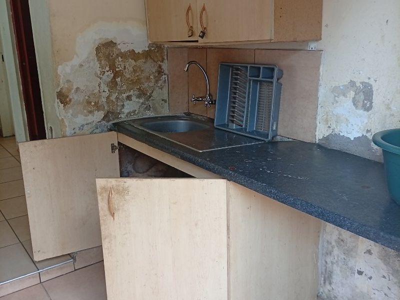 A small kitchen area featuring basic cabinetry and a sink, currently showing significant wall damage and requiring extensive renovation and repair.