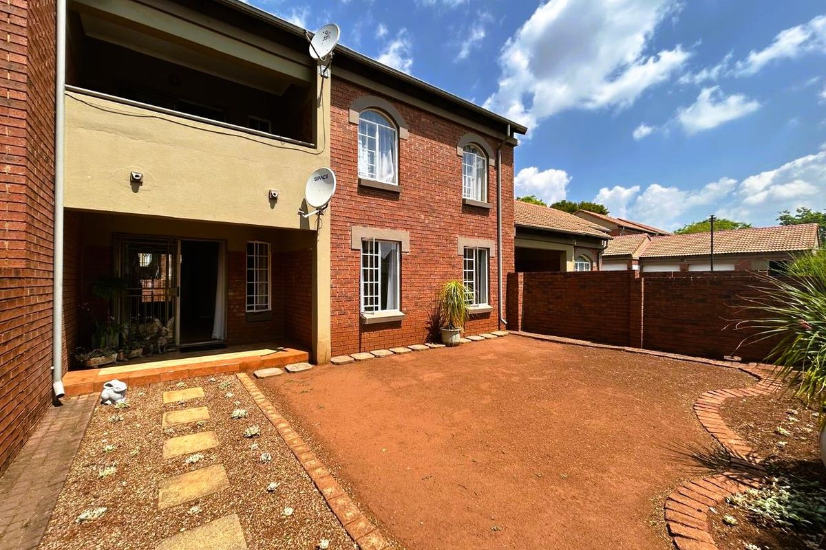 Rear view of a double-story brick apartment featuring a covered patio, arched windows, and a private garden area with paved pathways.