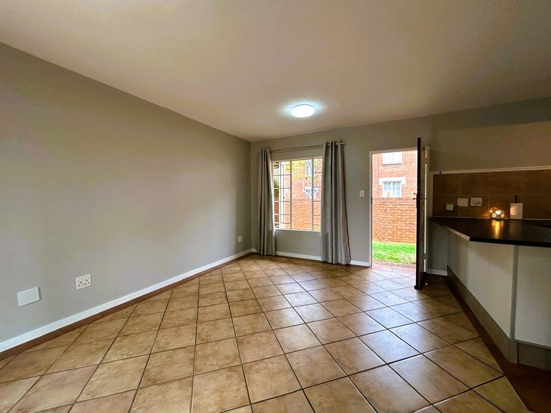 An open-plan living area featuring tiled flooring, a kitchen counter with a tiled backsplash, and direct access to an outdoor space.