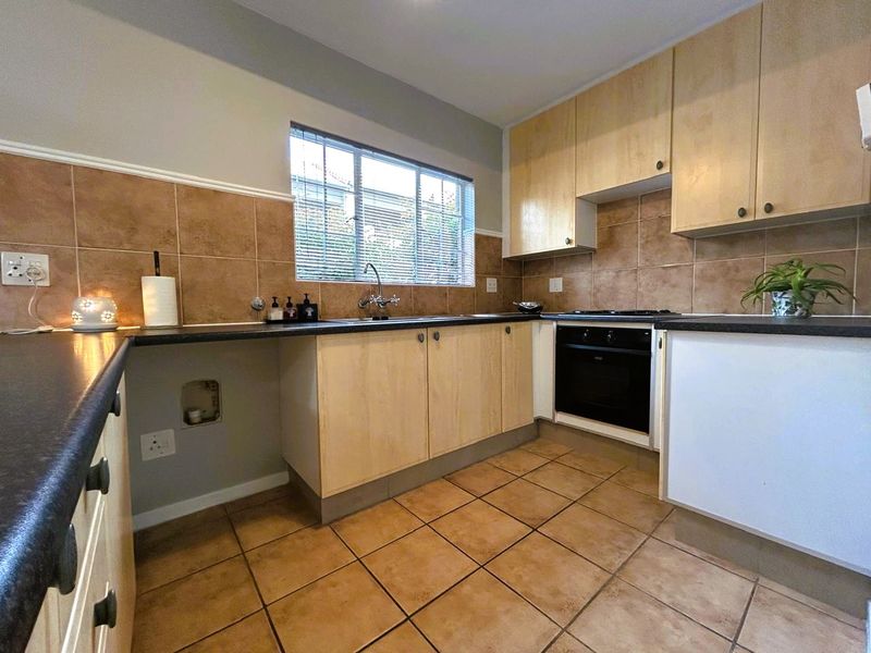 A functional kitchen featuring light wood cabinetry, dark laminate countertops, ceramic tile backsplash, and built-in oven with hob.