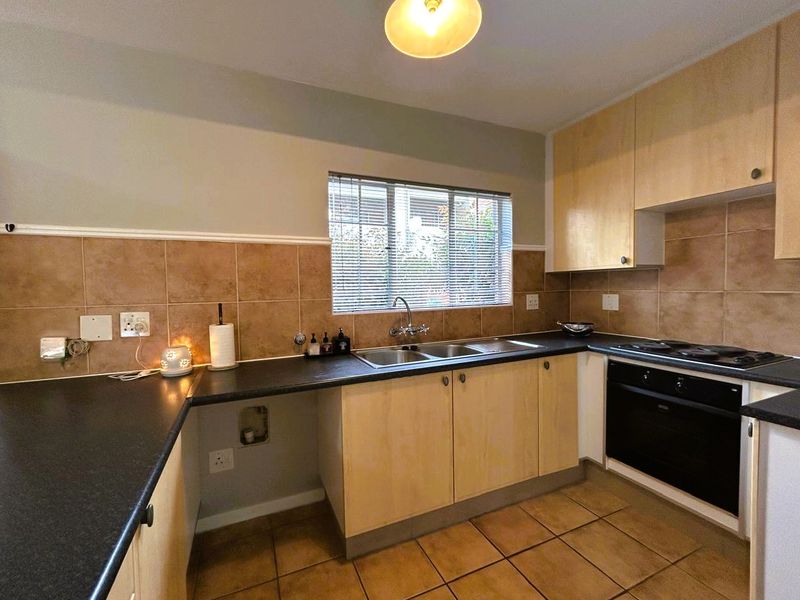 A functional kitchen featuring light wood-finish cabinetry, dark countertops, a built-in oven and hob, and tiled flooring with a neutral backsplash.