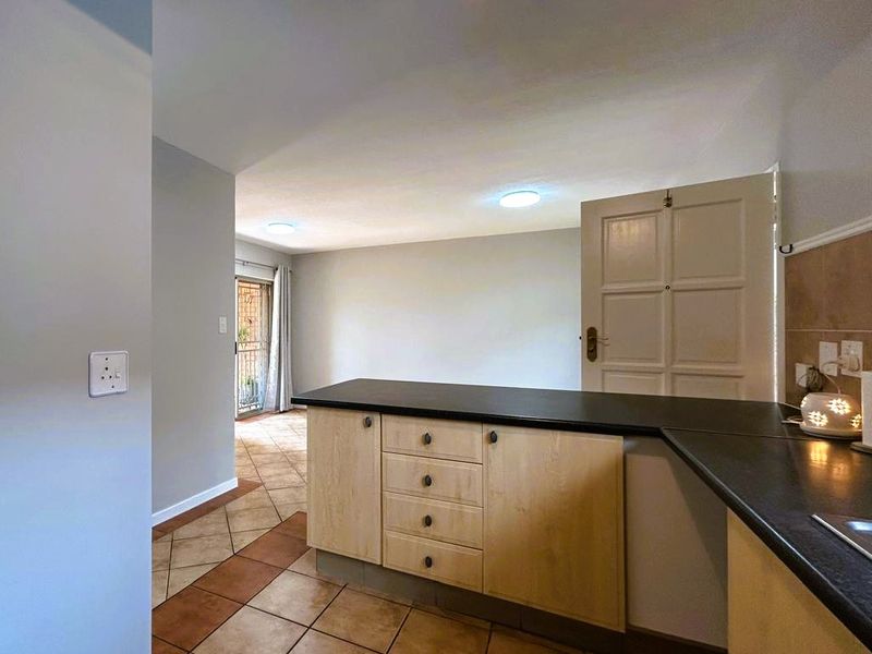 Open plan kitchen area featuring light wood cabinetry, dark countertops, and ceramic tiled flooring, leading into an adjacent living space.