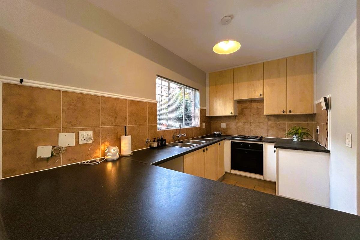 A functional kitchen featuring light wood cabinetry, dark laminate countertops, a double basin sink, and built-in oven and hob with tiled backsplash.