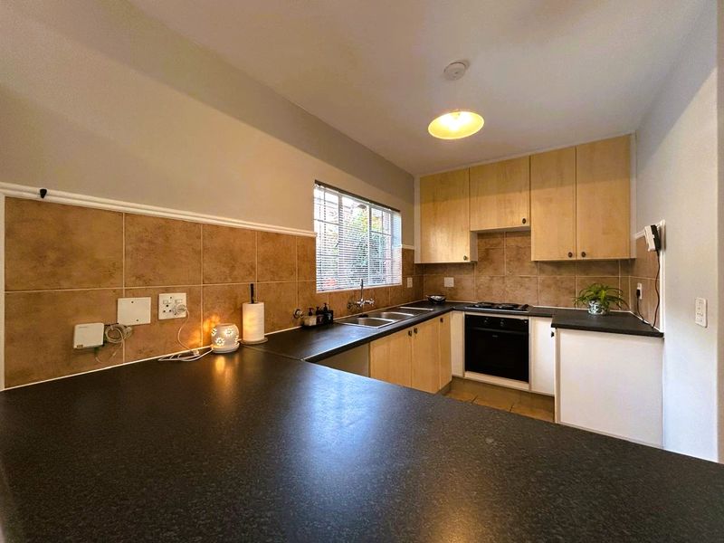 A functional kitchen featuring light wood cabinetry, dark laminate countertops, a double basin sink, and built-in oven and hob with tiled backsplash.