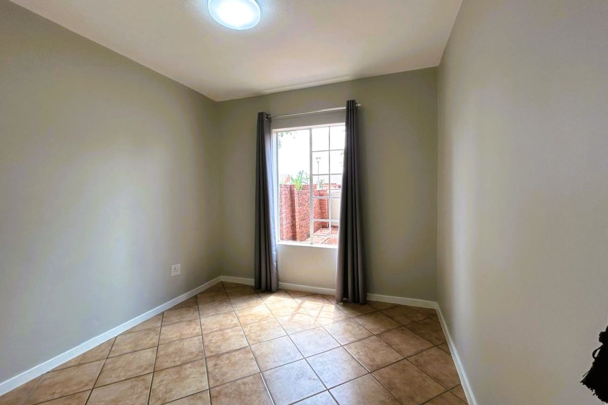 A vacant bedroom featuring neutral wall paint, ceramic tile flooring, and a window with security bars, offering a clean and versatile living space.