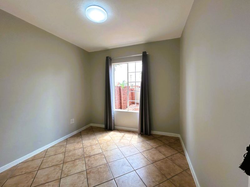 A vacant bedroom featuring neutral wall paint, ceramic tile flooring, and a window with security bars, offering a clean and versatile living space.