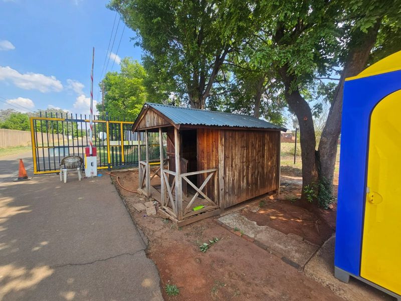 Front entrance area featuring a security gate, boom gate, and a small wooden shed structure on the property.