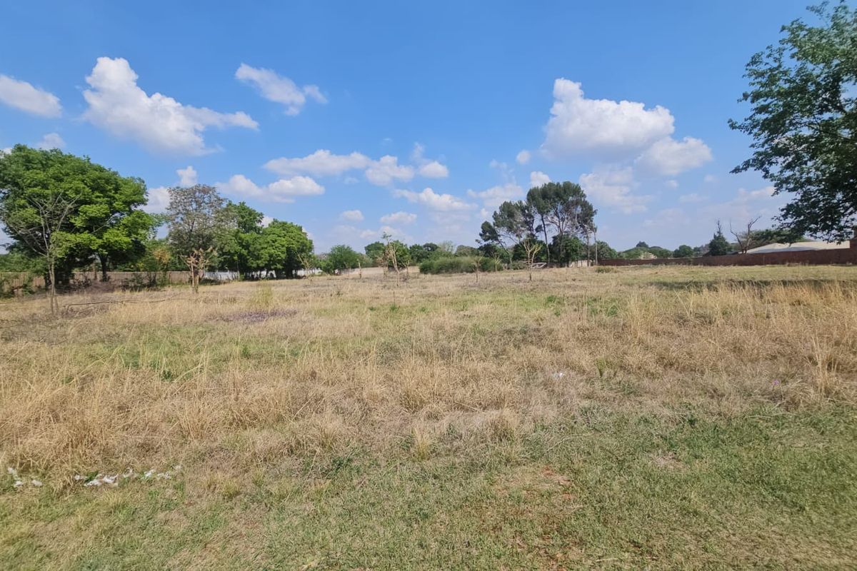 A spacious, level residential vacant land plot featuring established trees and natural grass cover, offering a blank canvas for future development.