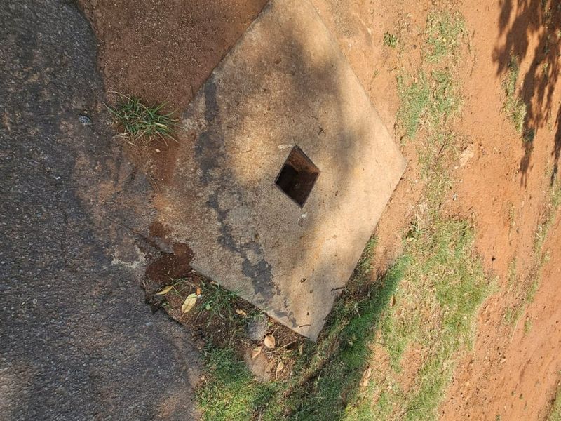 A close-up view of a utility access cover set into the ground on a vacant residential plot.