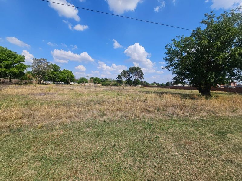 A wide-angle view of a vacant residential plot featuring established trees and open grassy terrain, suitable for future development.