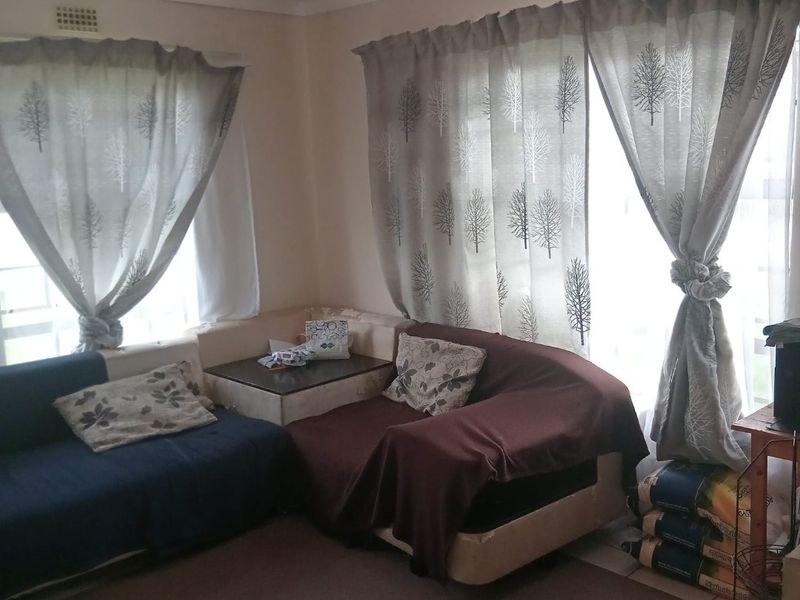 A living room area featuring corner wall detailing and large windows with curtain fixtures, requiring some cosmetic updates to the wall finishes.