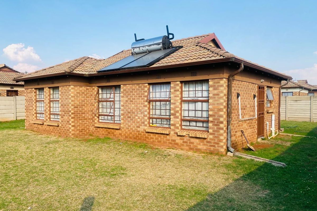 Rear view of a face brick house featuring a tiled roof with an integrated solar water heating system and steel-framed windows with security bars.