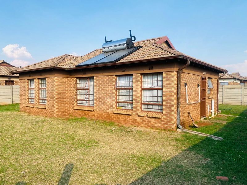 Rear view of a face brick house featuring a tiled roof with an integrated solar water heating system and steel-framed windows with security bars.