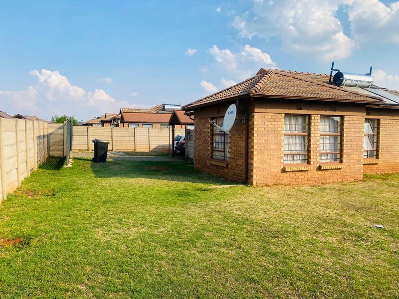 Rear view of a face brick house featuring a tiled roof, solar water heater, and a private garden enclosed by precast concrete boundary walls.