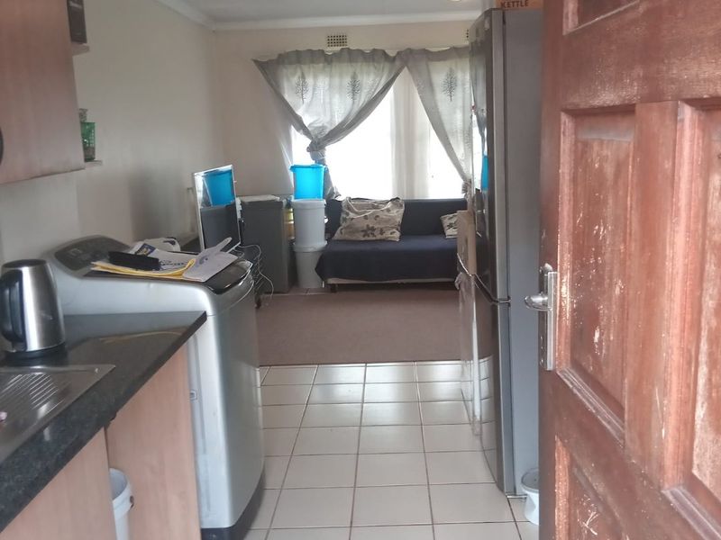 An open-plan living and kitchen area featuring tiled flooring and basic cabinetry, offering a functional layout that could benefit from cosmetic updates.