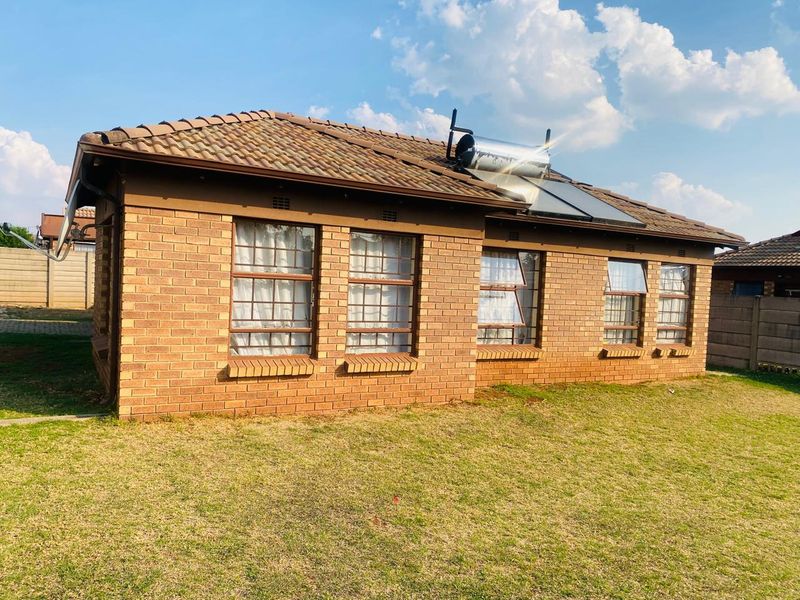 A rear view of a face brick house featuring a tiled roof with an installed solar water heating system and security-barred windows.