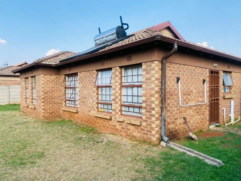 Rear exterior view of a face brick house featuring a tiled roof, solar water heating system, and secure steel-framed windows.